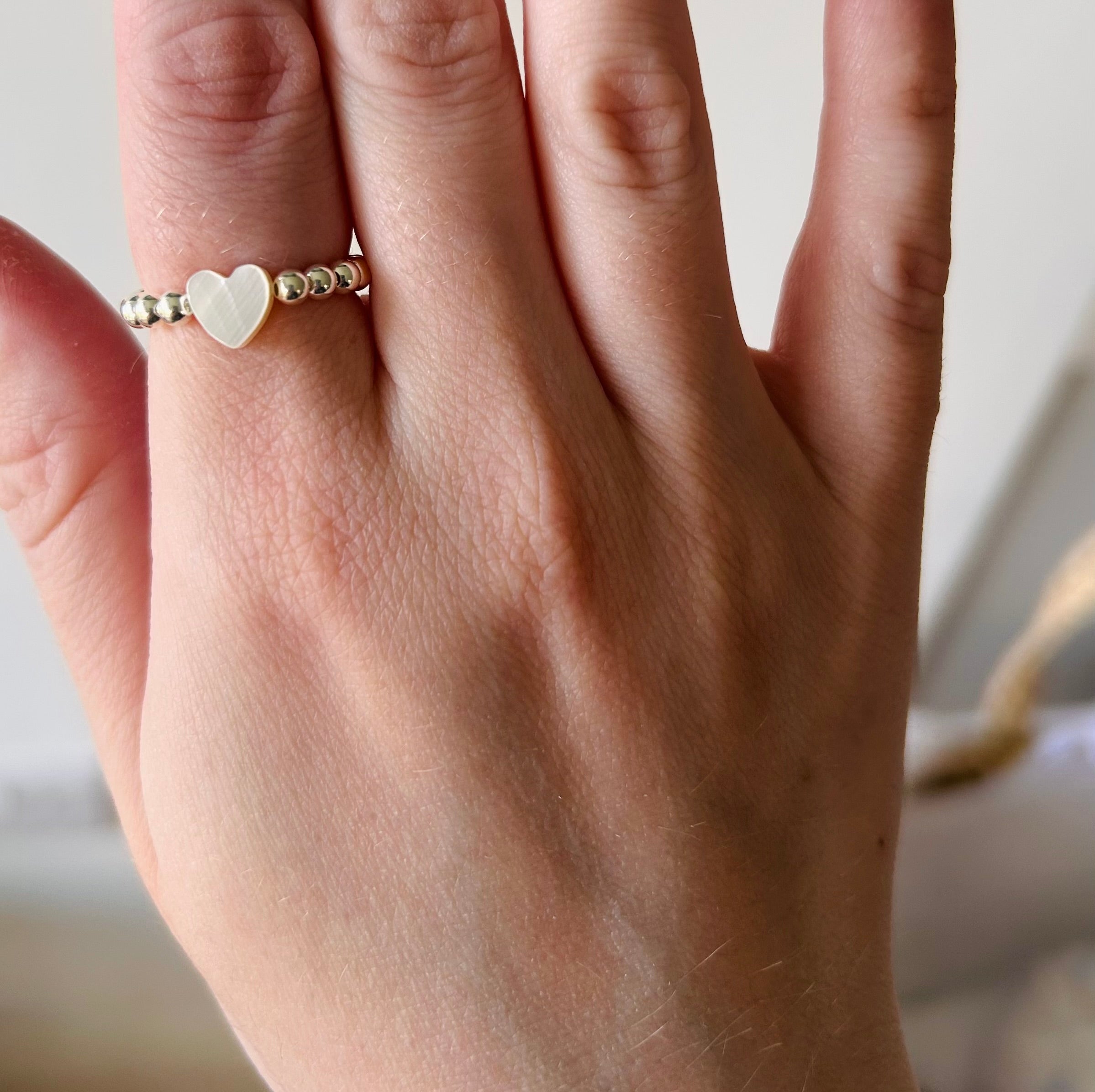 Hand wearing a gold ring with a heart-shaped stone on a neutral background