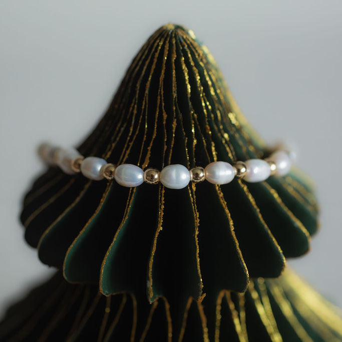 Pearl bracelet on a green and gold jewelry stand against a gray background