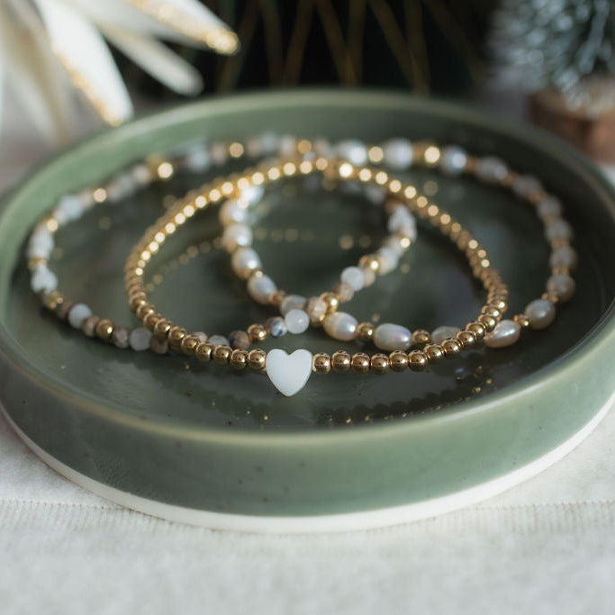Set of beaded bracelets on a green ceramic dish with a white background