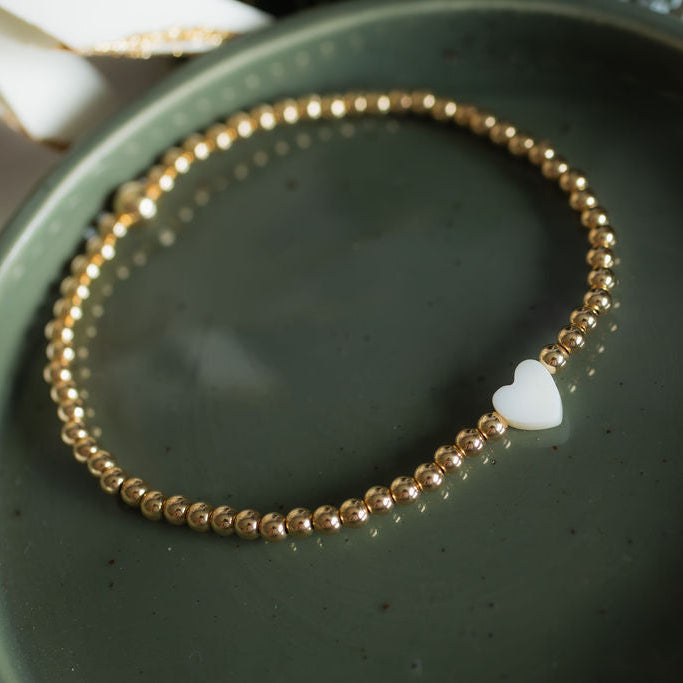 Gold beaded bracelet with a heart charm on a green surface