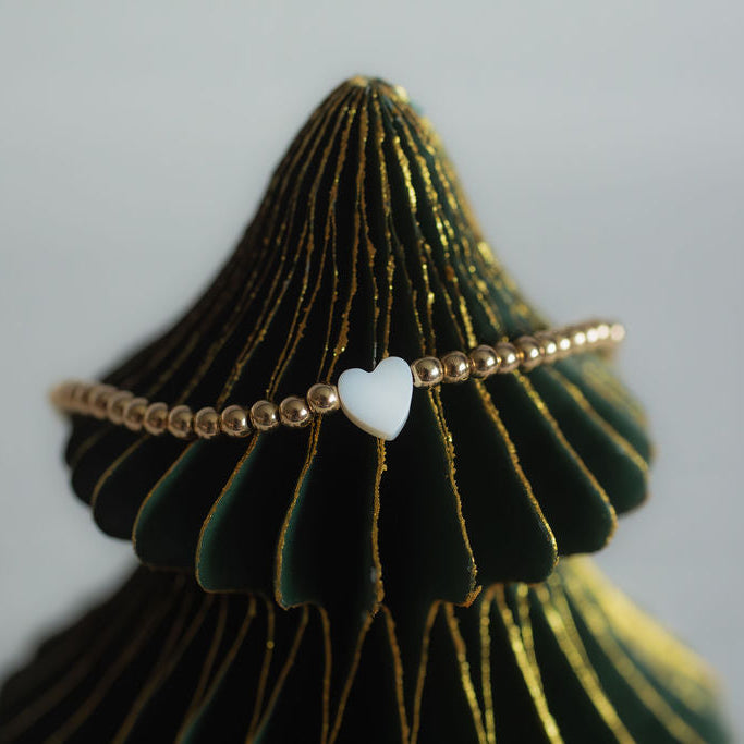 Bracelet with a heart charm on a green and gold textured stand